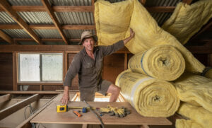 A homeowner in safety gear cutting roof insulation batts.